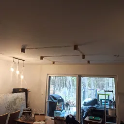 Nowoczesne oświetlenie sufitowe z drewnianymi oprawami punktowymi i wiszącą lampą z trzema żarówkami w minimalistycznym wnętrzu z widokiem na zewnątrz.