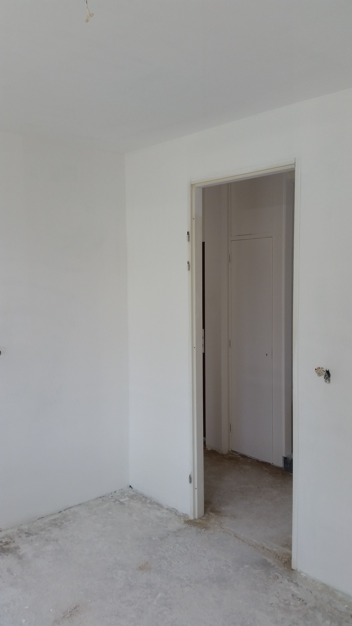 Pomalowane na biało ściany w pokoju z otwartymi drzwiami i niedokończoną podłogą, widoczne ślady po remoncie.
