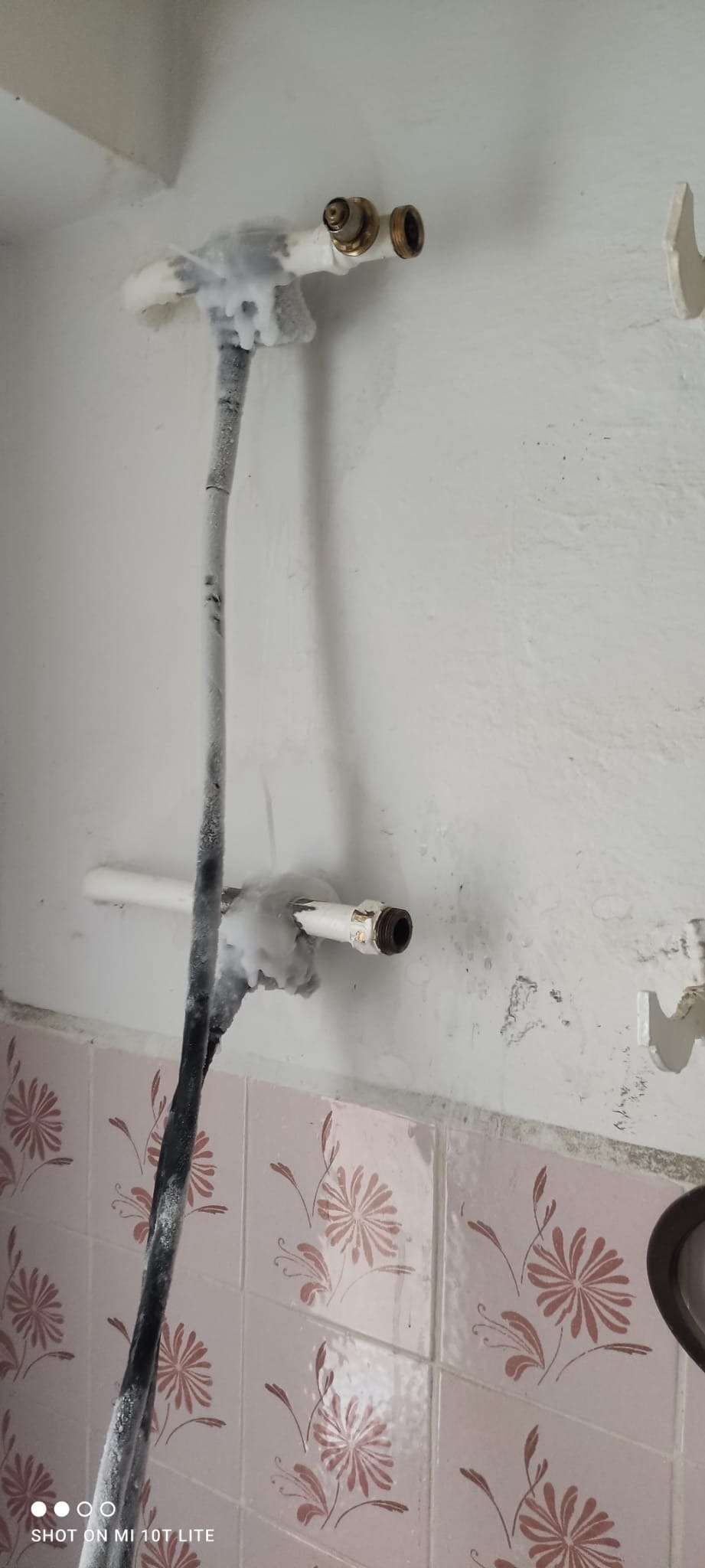 Zamrożone rury i zawory wodne w łazience z różowymi kwiatowymi płytkami, ukazujące potencjalne problemy z instalacją wodną zimą.