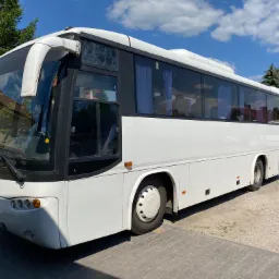 Biały autokar marki Marcopolo zaparkowany na placu z kostki brukowej, widok z przodu i boku, z widocznymi zasłonami w oknach.