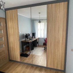 Szafa pod wymiar - Trzydrzwiowa szafa wnękowa z lustrami i drewnianymi bokami, szare obramowanie, widok na biurko z komputerem odbijające się w lustrach.