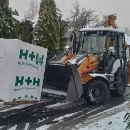 Pomarańczowa ładowarka CASE z paletą bloczków betonowych H+H na śnieżnej drodze w zimowy dzień.