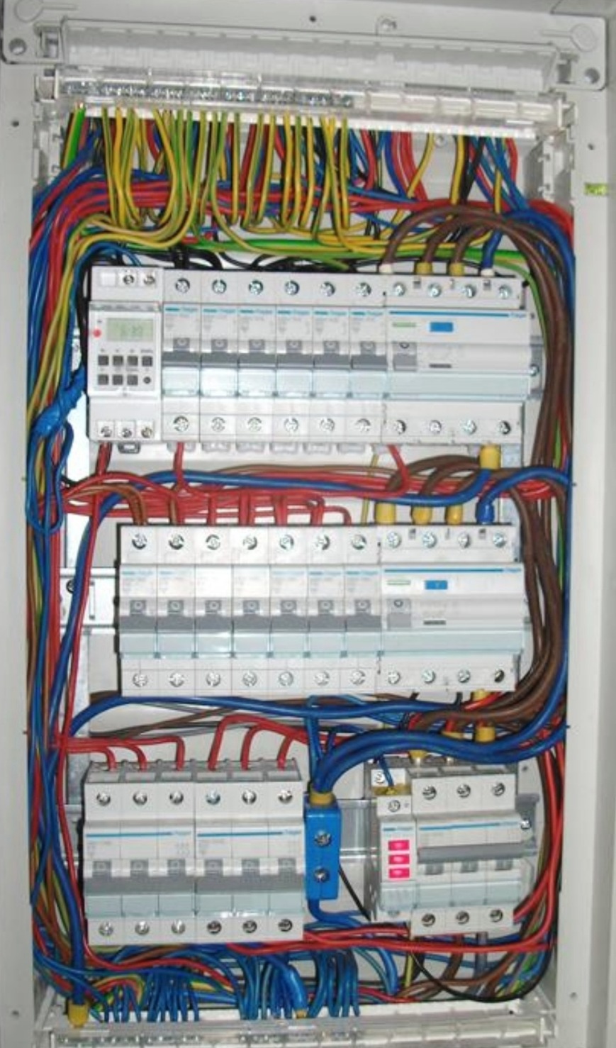 Rozdzielnia elektryczna z widocznymi bezpiecznikami, przewodami w różnych kolorach i programatorem czasowym.