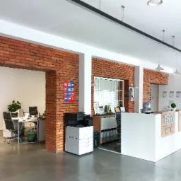 Nowoczesne biuro z recepcją, ściany z cegły, minimalistyczne meble biurowe i szklane drzwi.
