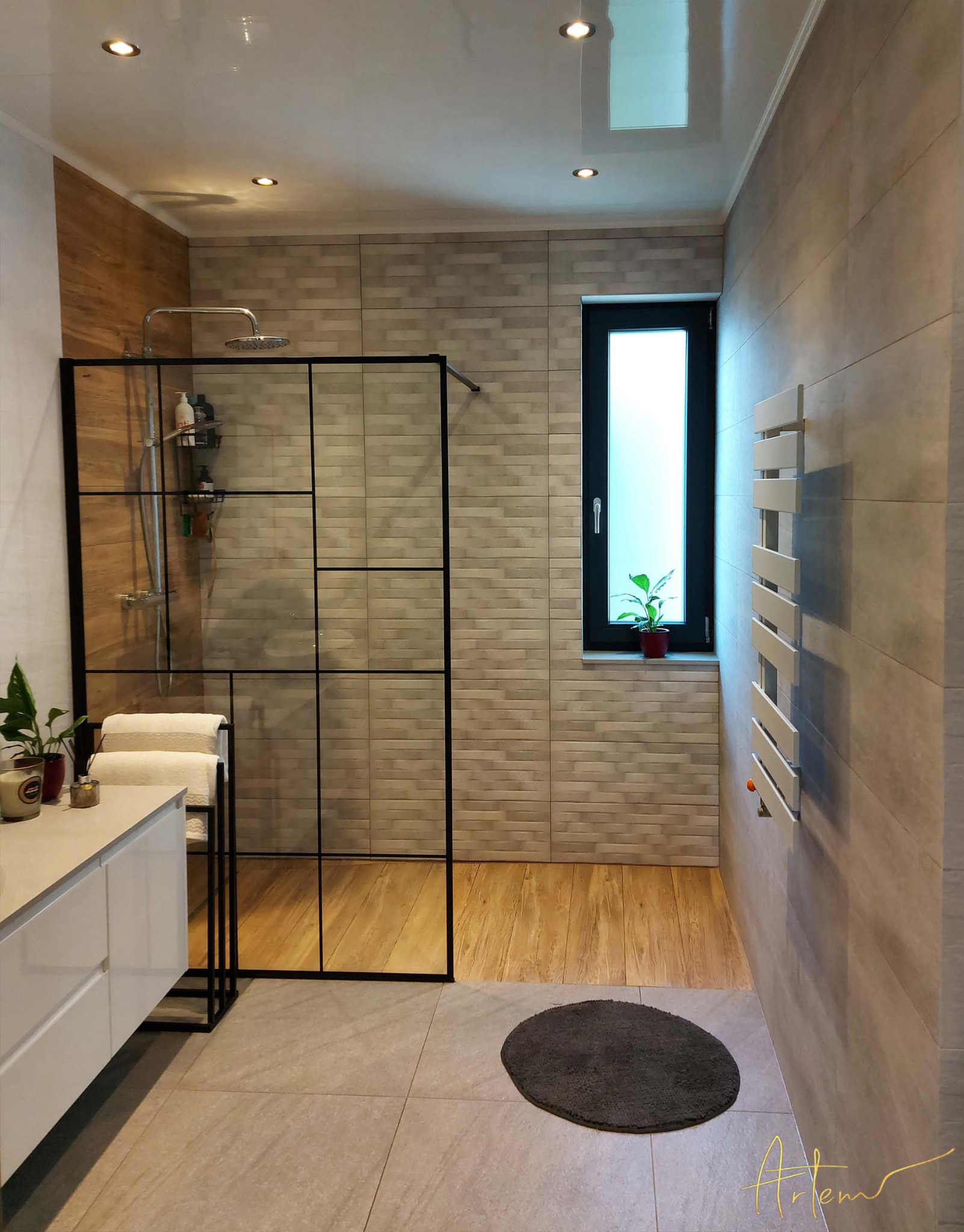 Nowoczesna łazienka z kabiną prysznicową typu walk-in z czarnymi szprosami, jasnymi płytkami imitującymi drewno na ścianach i podłodze, oraz białymi meblami łazienkowymi i grzejnikiem.