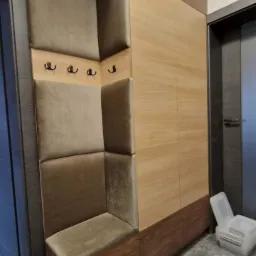 Wnęka z siedziskiem i wieszakami obita beżową tkaniną, wbudowana w drewnianą szafę w przedpokoju.