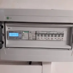 Otwarta skrzynka elektryczna z licznikiem zużycia energii Erstron SDM72D i wyłącznikami Eaton, zamontowana na ścianie.