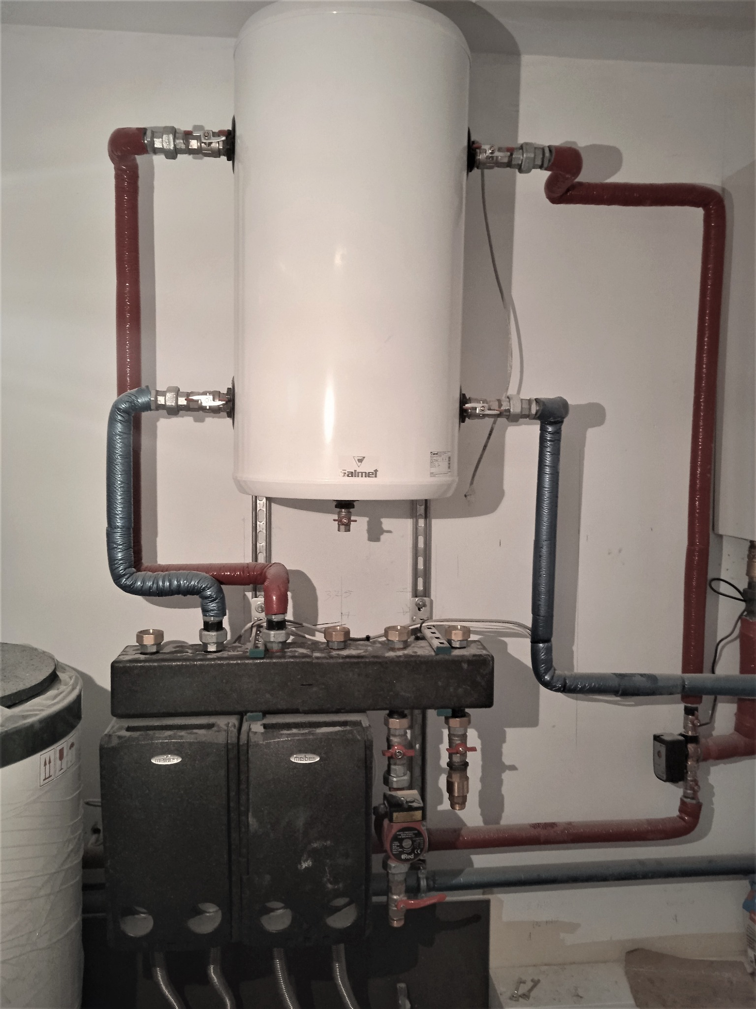 Bojler marki Galmet z podłączeniami rur miedzianych w izolacji oraz moduł hydrauliczny Meibes, zamontowane na białej ścianie.