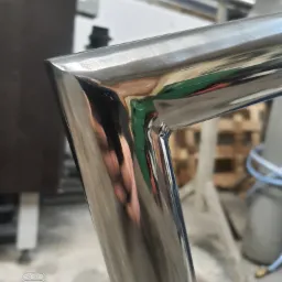 Detal spawu narożnego ramy z polerowanej stali nierdzewnej, widoczne odbicia otoczenia, w tle warsztat.