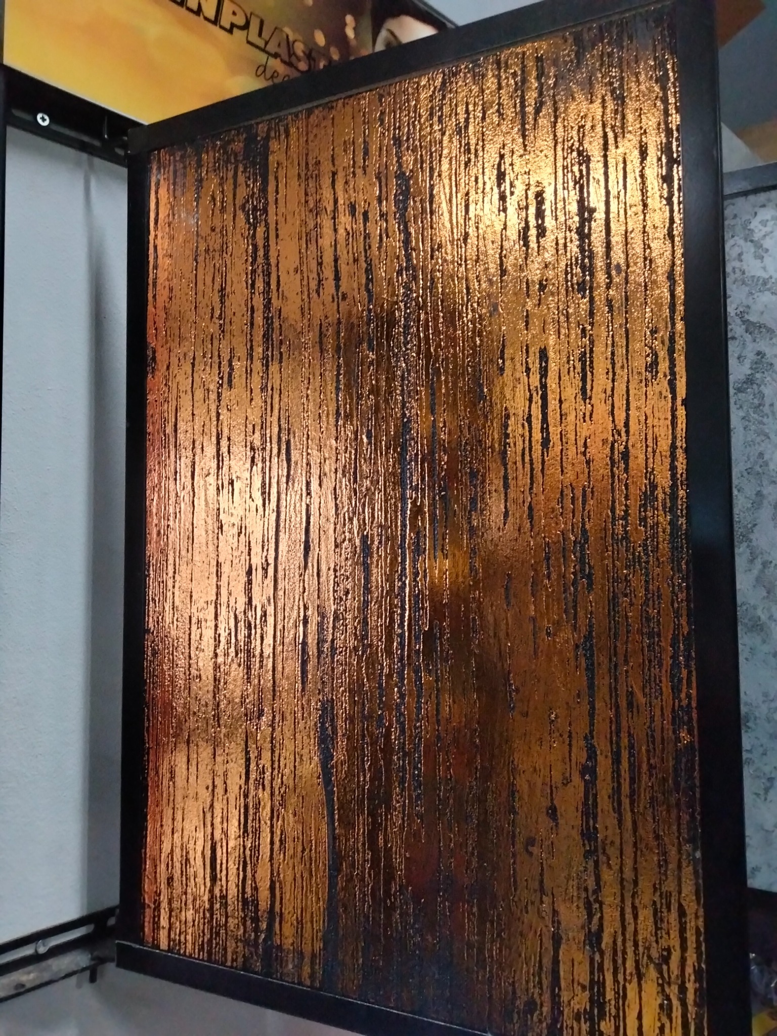 Panel dekoracyjny z efektem miedzianych zacieków w czarnej ramie, oświetlony od góry, prezentowany w pionie. Unikalna faktura i gra świateł.