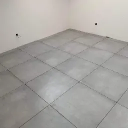 Szare płytki podłogowe ułożone na krzyż ze szpachelkami dystansowymi w pomieszczeniu we Wrocławiu, widoczne gniazdka elektryczne na ścianie.