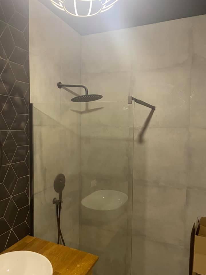 Nowoczesna kabina prysznicowa z deszczownicą w kolorze grafitowym, szklana ściana działowa, umywalka nablatowa i geometryczne płytki na ścianie.