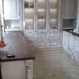 Kuchenna zabudowa w stylu rustykalnym z przeszklonymi szafkami podświetlonymi od wewnątrz, drewniany blat i kolumna dekoracyjna.