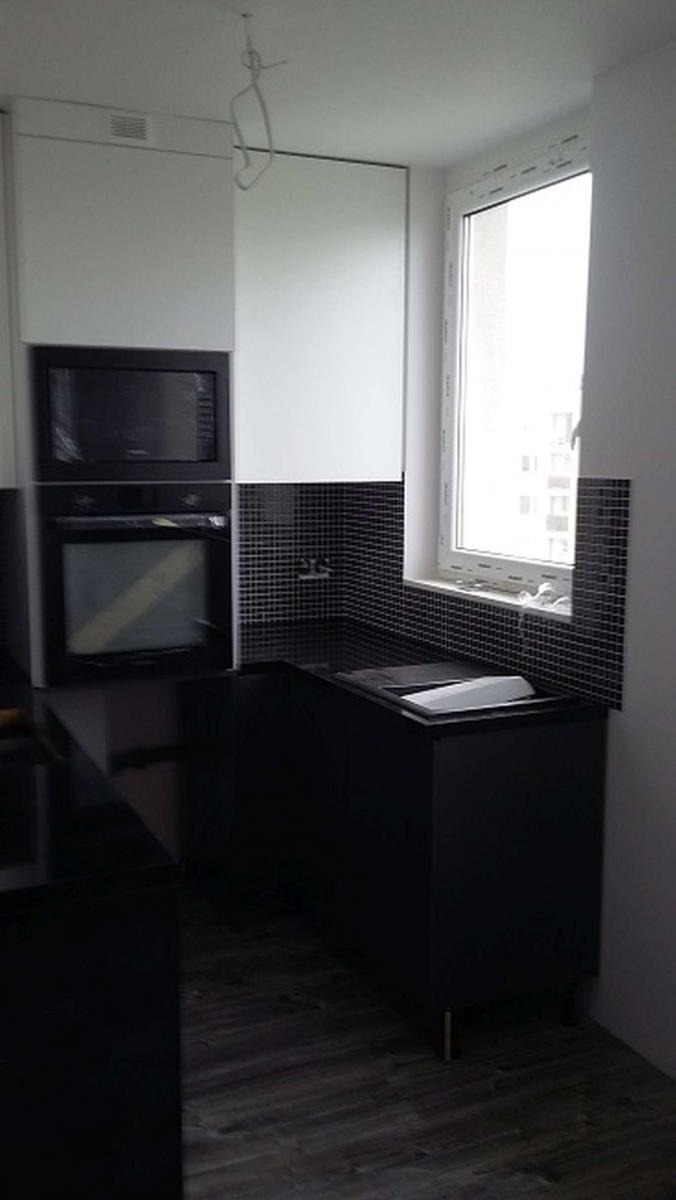 Nowoczesna kuchnia w trakcie montażu: czarne szafki dolne z błyszczącym blatem, białe szafki górne, czarna mozaika na ścianie, widoczne przewody pod sufitem.