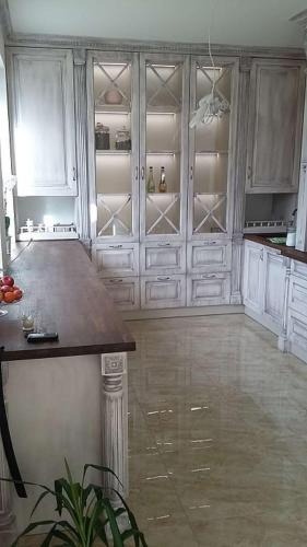 Kuchenna zabudowa w stylu rustykalnym z przeszklonymi szafkami podświetlonymi od wewnątrz, drewniany blat i kolumna dekoracyjna.