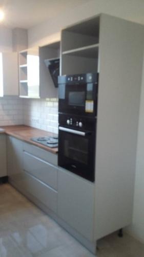 Jasnoszara zabudowa kuchenna z drewnianym blatem, piekarnikiem w zabudowie i białymi płytkami na ścianie.