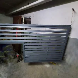 Szara, metalowa brama wjazdowa z poziomymi szczeblami, częściowo ukończona, widoczna w warsztacie z narzędziami w tle.