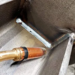 Zbliżenie na proces spawania metalowej konstrukcji, widoczne spoiwo i uchwyt spawalniczy