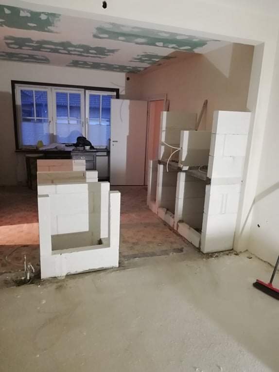 Wnętrze w trakcie budowy: surowy strop z widocznymi łatami gipsowymi, ściany w stanie surowym, a na podłodze i wzdłuż ściany konstrukcje z białych bloczków, prawdopodobnie przygotowywane...