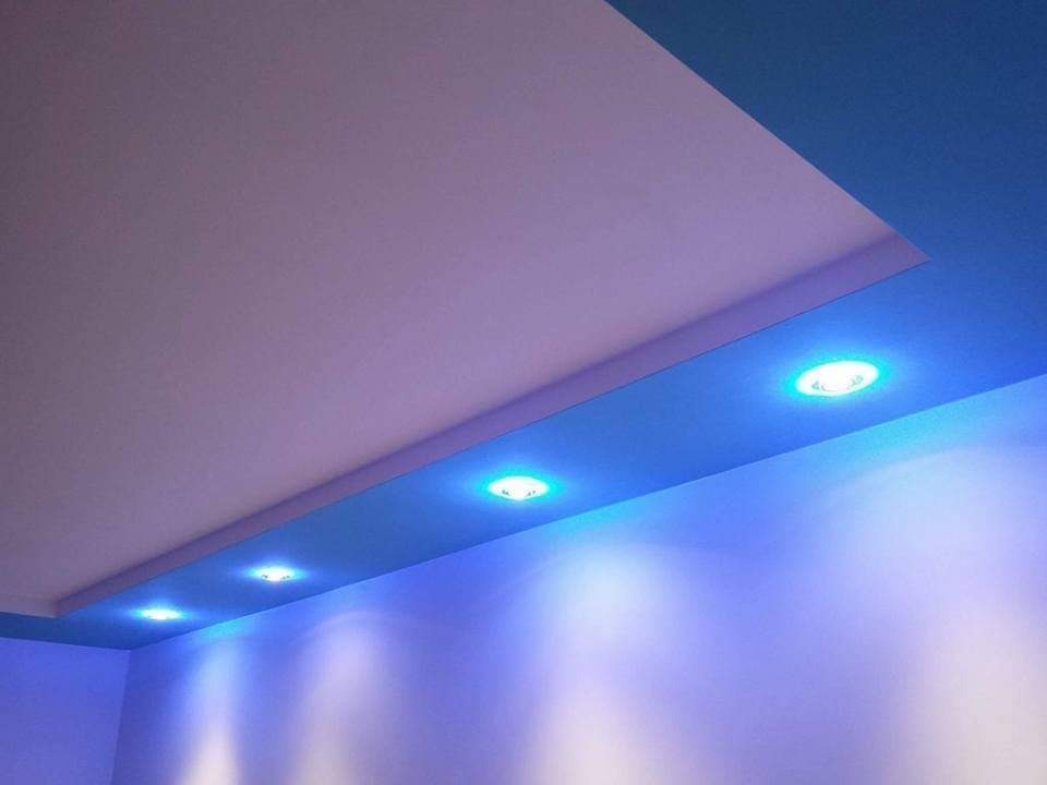 Dwupoziomowy sufit podwieszany z wbudowanymi punktowymi źródłami światła LED, emitującymi niebieską poświatę na ścianę.