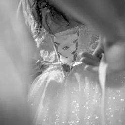 Czarno-białe zbliżenie na plecy panny młodej w błyszczącej sukni, sznurowanej białymi wstążkami, kt&oacute;re ktoś właśnie zawiązuje.