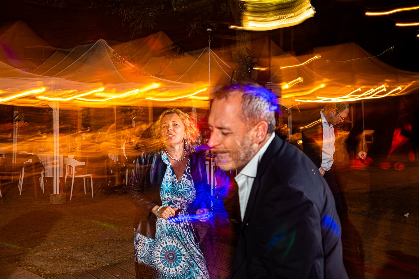 Para tańczy na parkiecie oświetlonym dekoracyjnymi lampami podczas wieczornego przyjęcia.