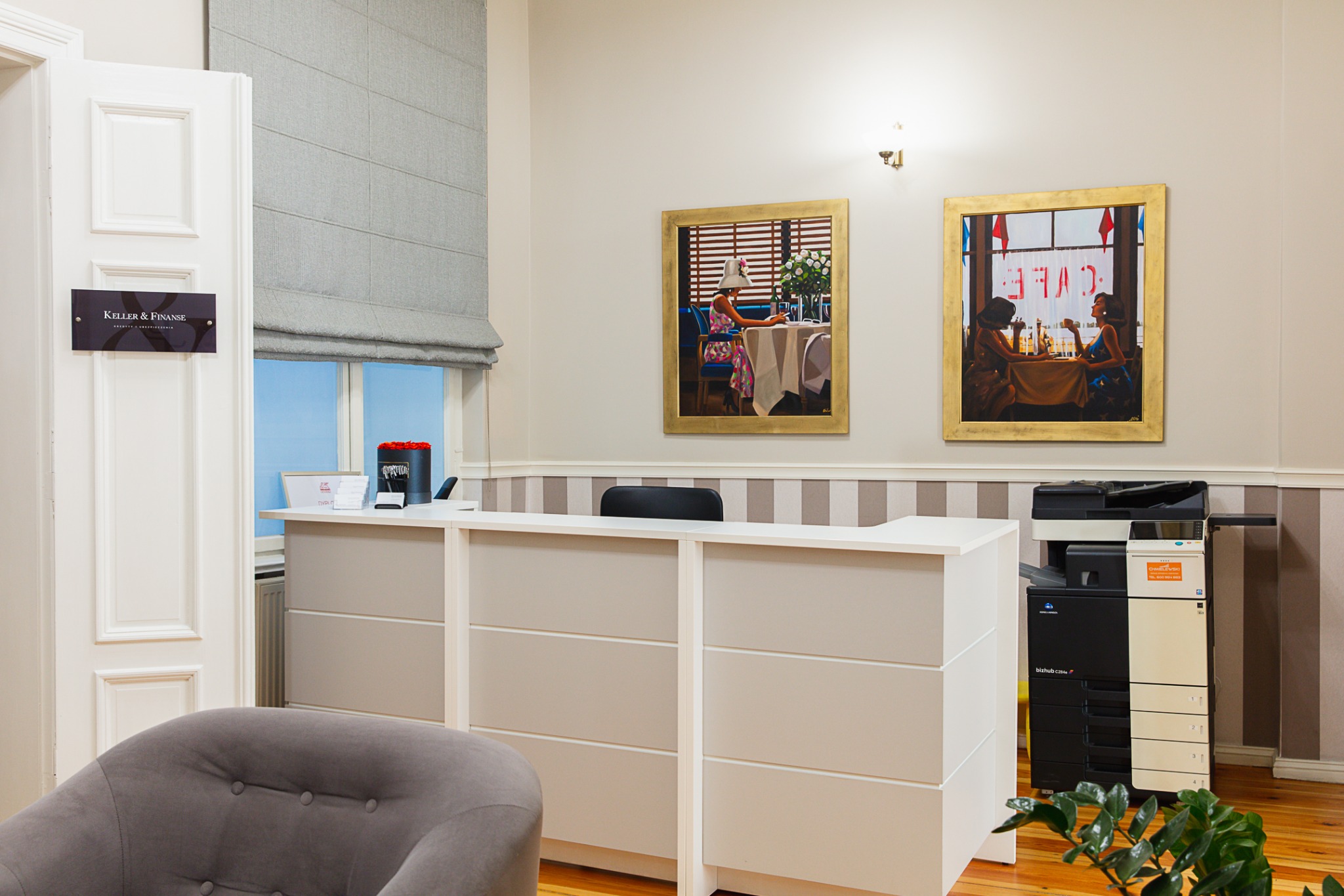Recepcja biura kredytowego z obrazami w złotych ramach, szarym krzesłem i drukarką wielofunkcyjną.