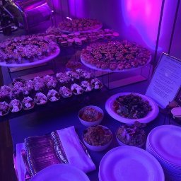 Siódemki - Bufet z przekąskami na stole podświetlonym fioletowym światłem, widoczne talerze z różnorodnymi przystawkami, miseczki z dipami, stosy talerzy i sztućce.