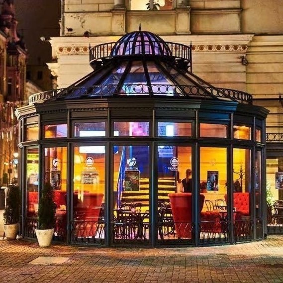 Elegancka, przeszklona weranda restauracji z dekoracyjną kopułą, widoczna z zewnątrz nocą, z oświetleniem wewnętrznym tworzącym ciepłą atmosferę.
