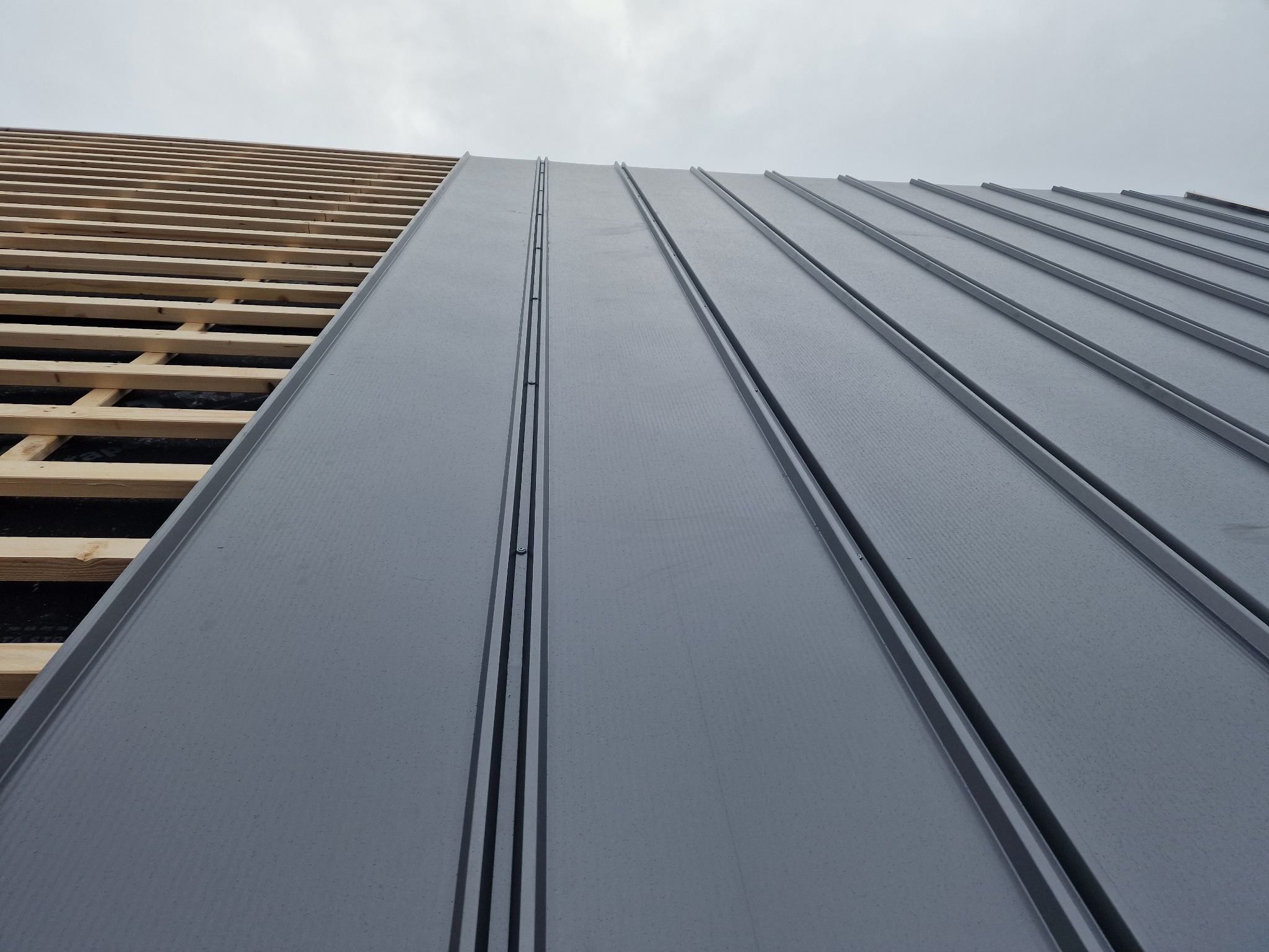 Montaż paneli blaszanych na konstrukcji drewnianej dachu, widoczne krople wody na powierzchni.