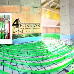 Rozłożone pętle ogrzewania podłogowego z zielonych rur na folii z nadrukowaną siatką, widoczny rozdzielacz w białej szafce, logo firmy na ścianie, surowy stan budynku.