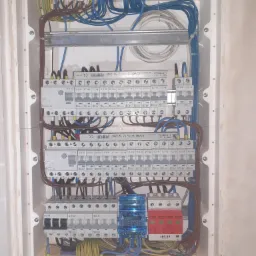 Rozdzielnia elektryczna w białej obudowie, widoczne bezpieczniki EATON, listwy zaciskowe, przewody w różnych kolorach (niebieski, brązowy, żółto-zielony), zabezpieczenie przepięciowe ADELID...