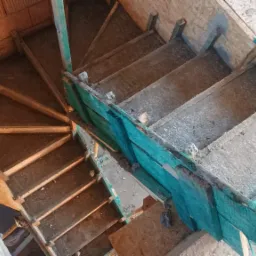 Wewnętrzne schody spiralne w trakcie wylewania betonu, widoczne szalunki z desek i płyty OSB, surowy stan wykończenia.