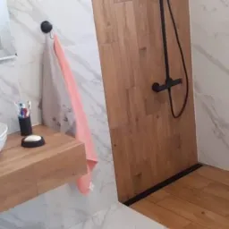 Nowoczesna łazienka z umywalką o fakturze muszli, czarną armaturą, marmurowymi płytkami i kabiną prysznicową wykończoną drewnem.