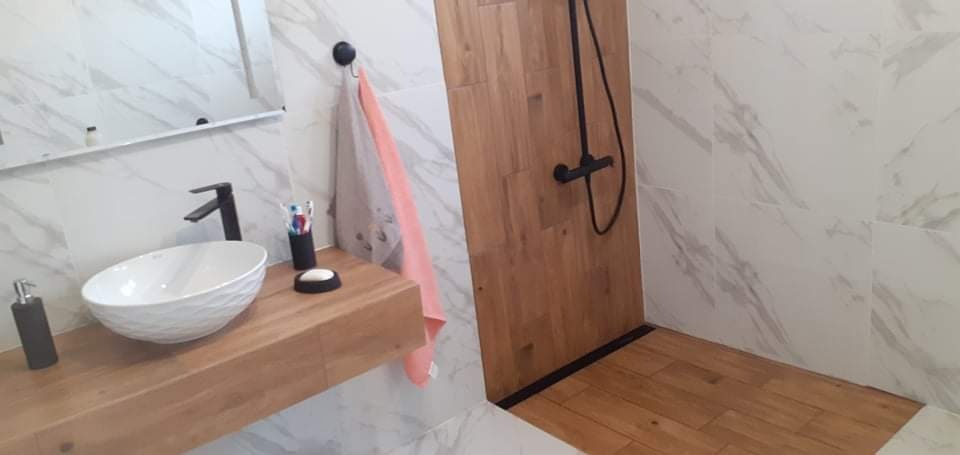 Nowoczesna łazienka z umywalką o fakturze muszli, czarną armaturą, marmurowymi płytkami i kabiną prysznicową wykończoną drewnem.