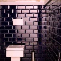 Mutacja Weronika Cwanek - Nowoczesna łazienka w hotelu Kazimierz w Krakowie: biała, kwadratowa toaleta podwieszana na tle ściany z błyszczących, granatowych płytek typu metro, z pojedynczą białą płytką dla akcentu...