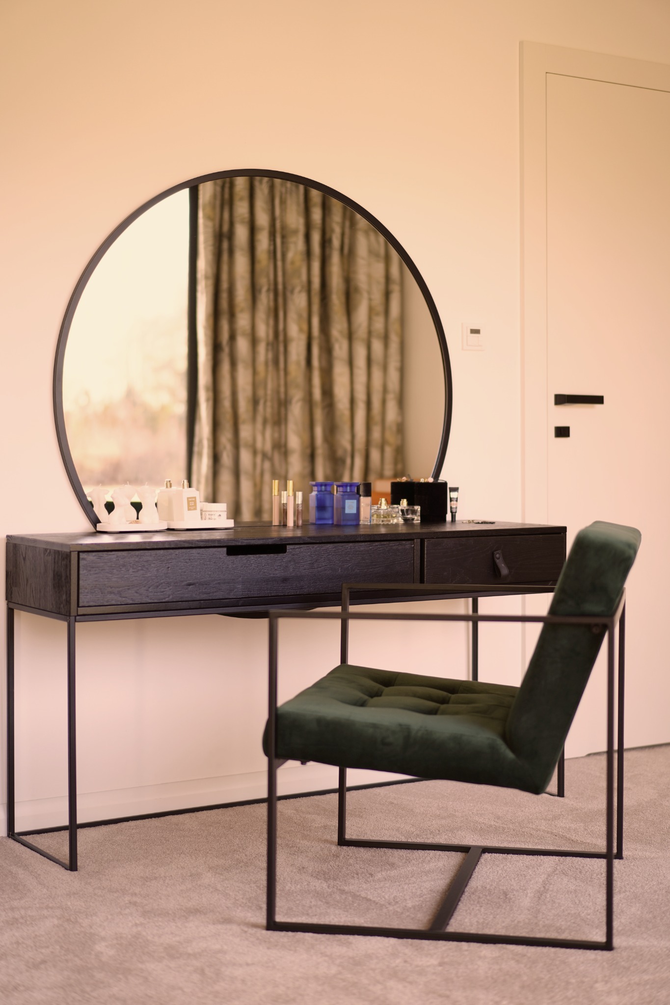 Toaletka z okrągłym lustrem, czarnym blatem i zielonym, tapicerowanym krzesłem na metalowym stelażu, na blacie kosmetyki i świece.