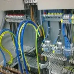 Rozdzielnica elektryczna z widocznymi przewodami w kolorach niebieskim i żółtym, szynami zbiorczymi, bezpiecznikami i listwami zaciskowymi.