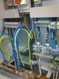 Rozdzielnica elektryczna z widocznymi przewodami w kolorach niebieskim i żółtym, szynami zbiorczymi, bezpiecznikami i listwami zaciskowymi.
