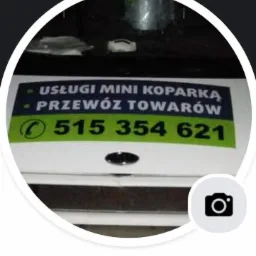 Reklama usług mini koparką i przewozu towarów z numerem telefonu 515 354 621, umieszczona na białej powierzchni, widoczna w okrągłym obramowaniu.