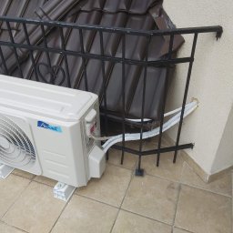 Maxcold Sp. z o.o. - Biała jednostka zewnętrzna klimatyzatora marki Airwell zamontowana na balkonie z ciemną balustradą i brązowymi dachówkami w tle.