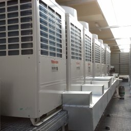 Maxcold Sp. z o.o. - Rząd białych jednostek zewnętrznych klimatyzacji Toshiba SHRM-e ustawionych na dachu budynku komercyjnego, widok perspektywiczny z boku, z widocznymi kratkami wentylacyjnymi i elementami instalacji.