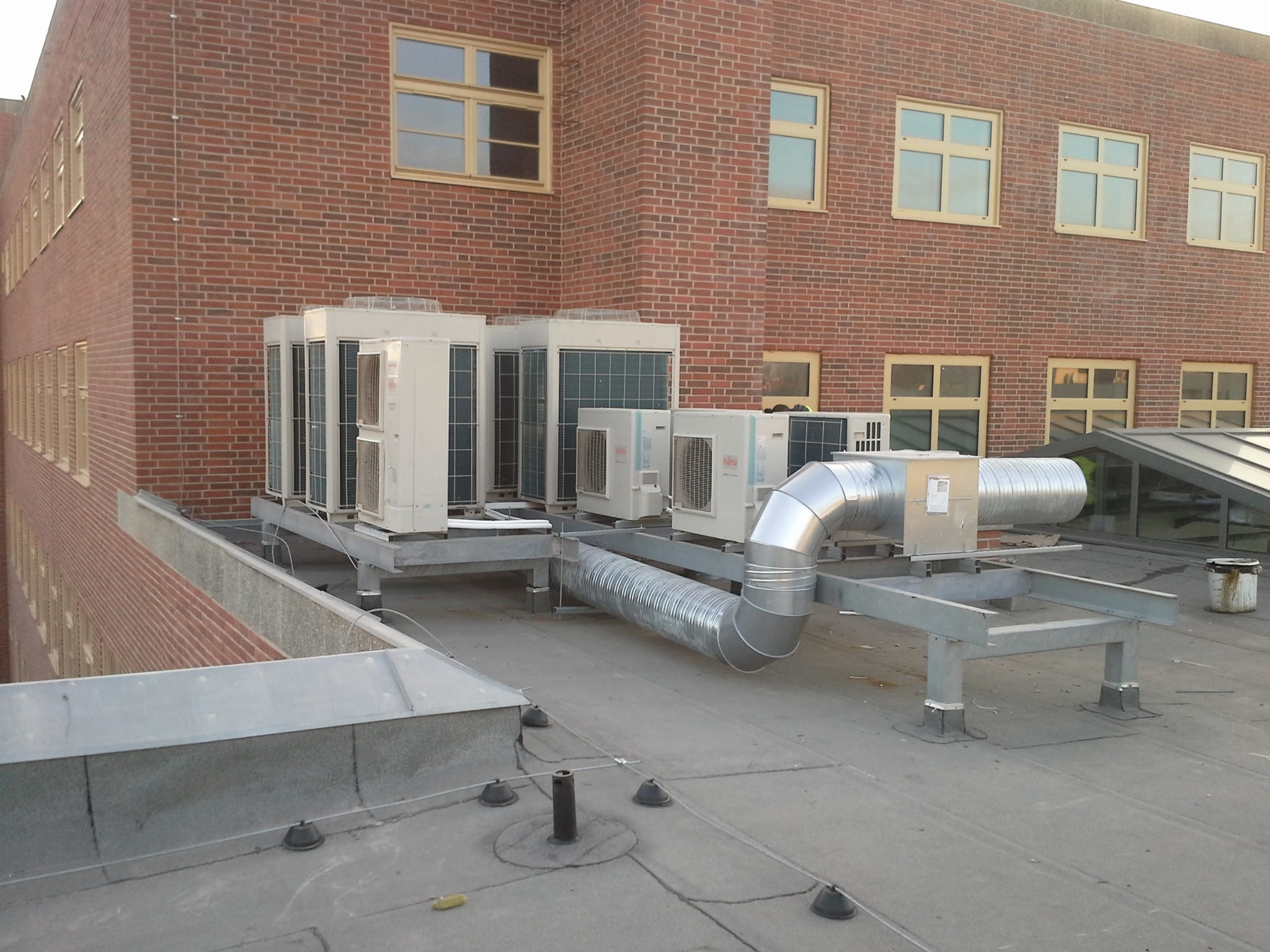 Zewnętrzne jednostki klimatyzacyjne na dachu budynku z cegły, połączone metalowymi kanałami wentylacyjnymi.