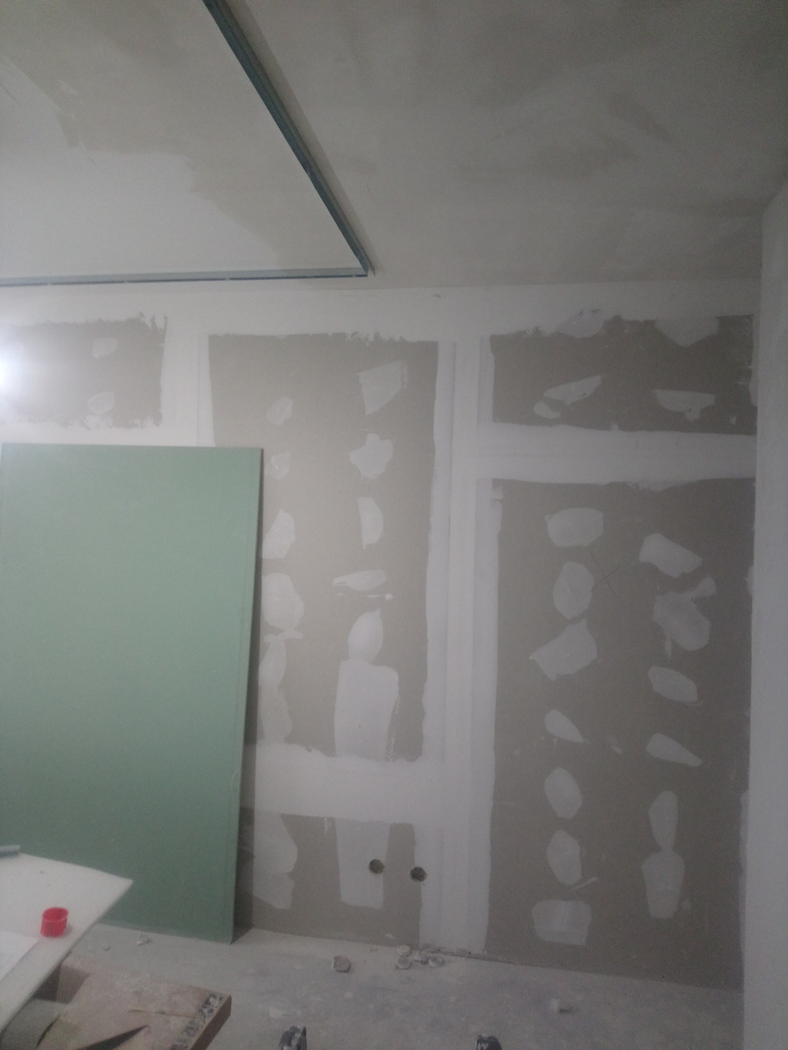 Wnętrze w trakcie prac wykończeniowych: ściany z nałożoną warstwą gipsu, widoczne łączenia płyt kartonowo-gipsowych, profil sufitowy zamontowany w górnej części kadru, niezabudowana płyta g-k...