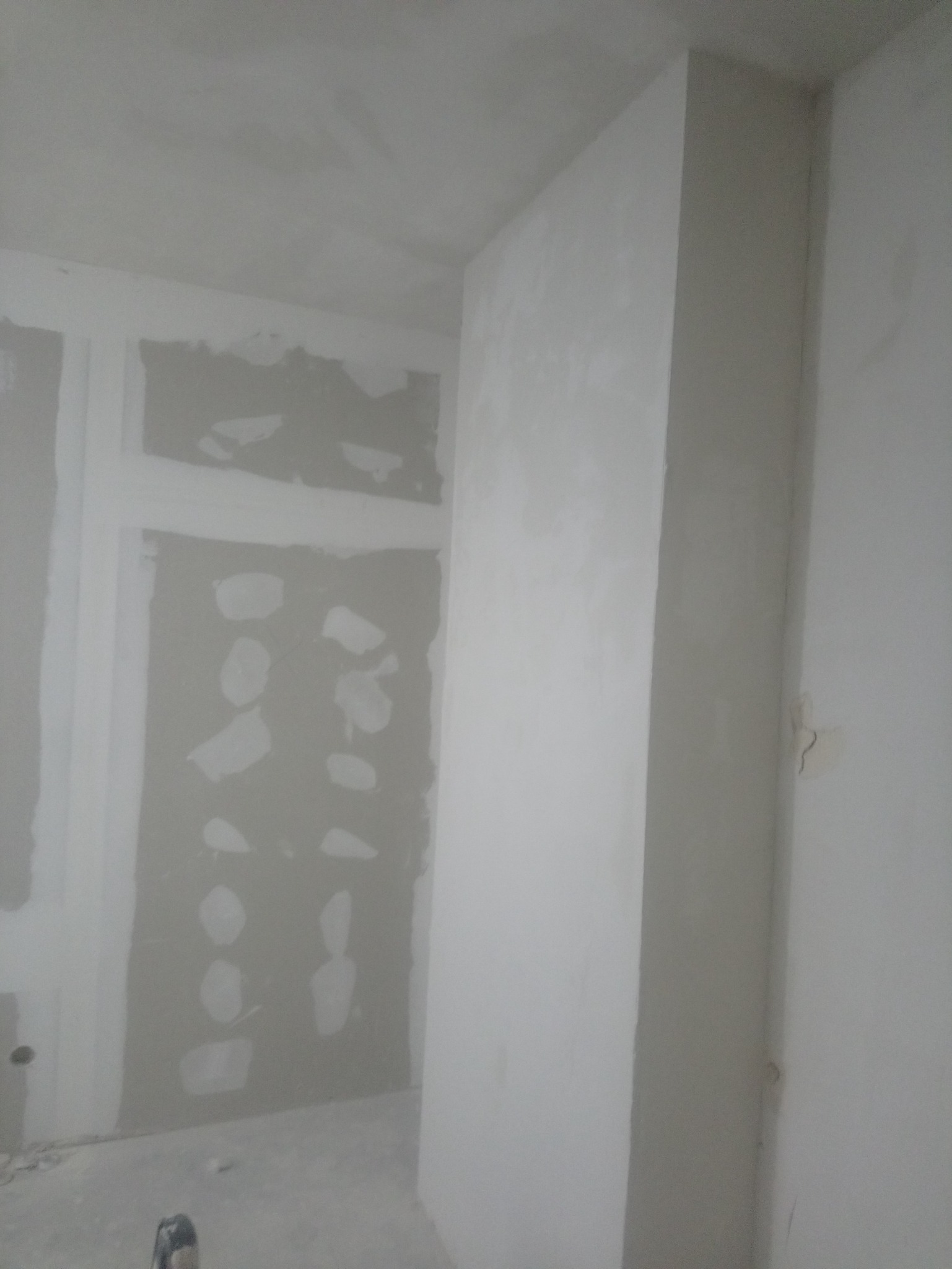 Ściana z płyt kartonowo-gipsowych w trakcie szpachlowania, widoczne nierówności i miejsca łączeń płyt, pionowy słup z płyt KG po prawej stronie.