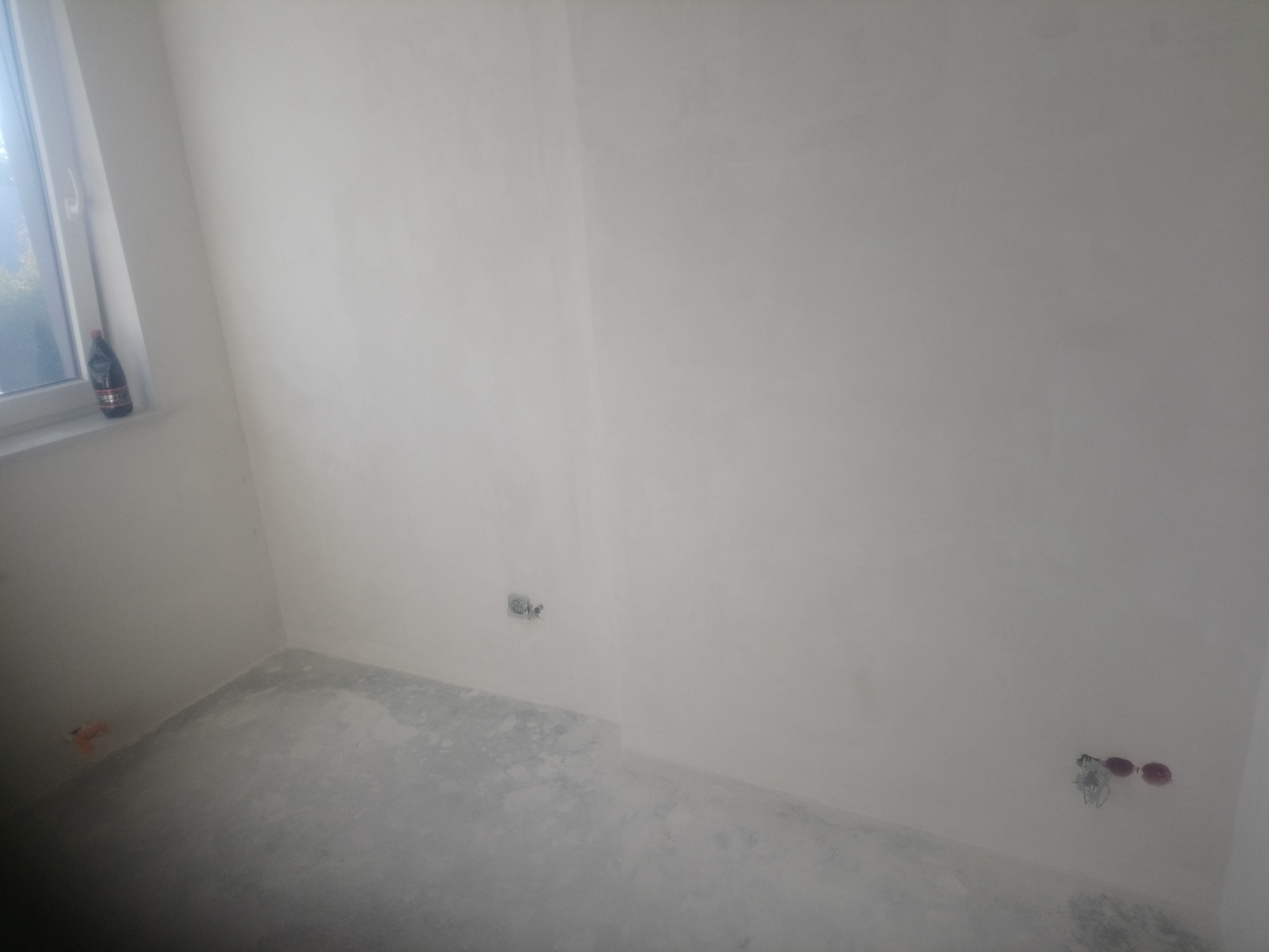 Pokój po gładziowaniu ścian i wylewce podłogi, widoczne puszki elektryczne, butelka płynu na parapecie.
