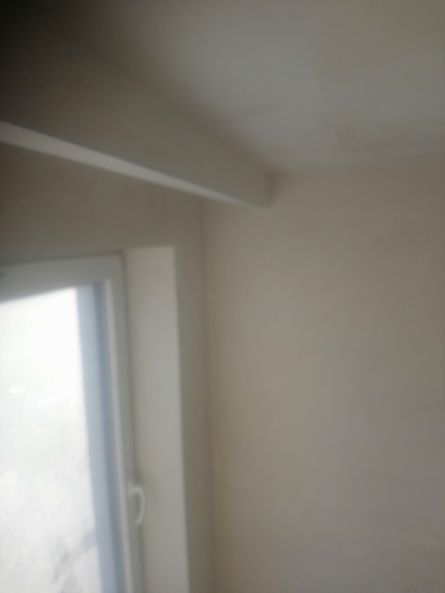 Fragment pokoju po malowaniu ścian na jasny kolor, widoczny narożnik, okno i listwa sufitowa.