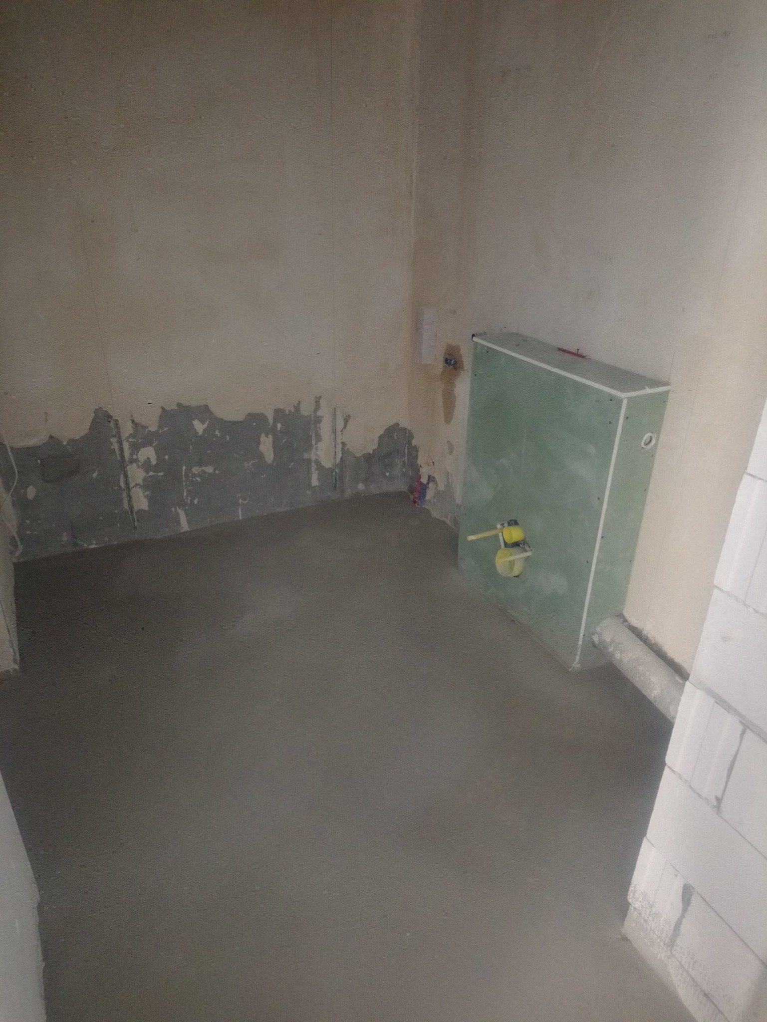 Surowy stan łazienki w trakcie prac: wylewka podłogowa, obudowa stelaża WC z płyt karton-gips, ściany z widocznymi śladami po skuciu starej glazury.