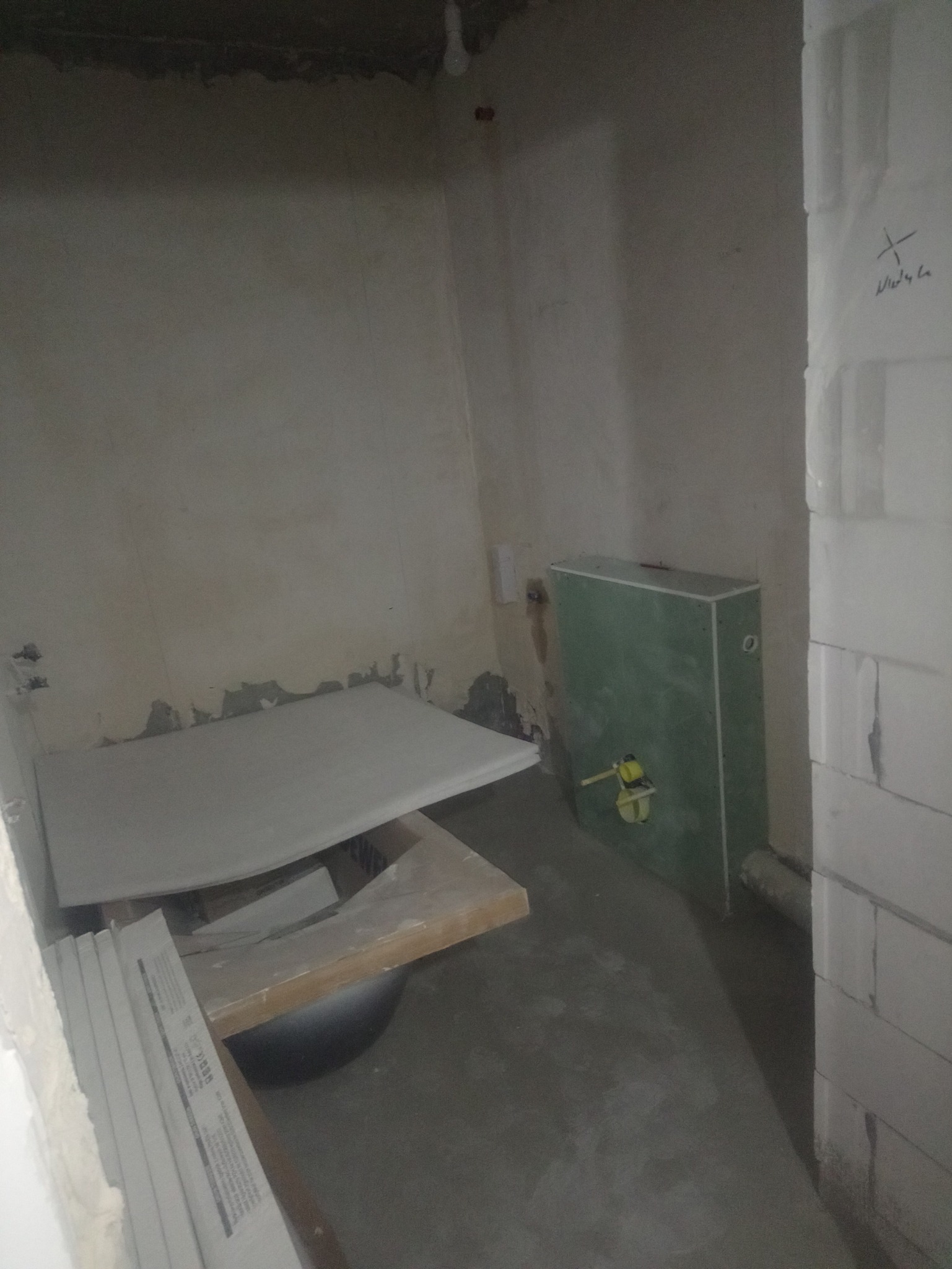 Niedokończona łazienka w trakcie prac: zabudowa stelaża WC z płyty GK, płyty gipsowe ułożone na prowizorycznym stole, surowe ściany, widoczna instalacja wodno-kanalizacyjna.