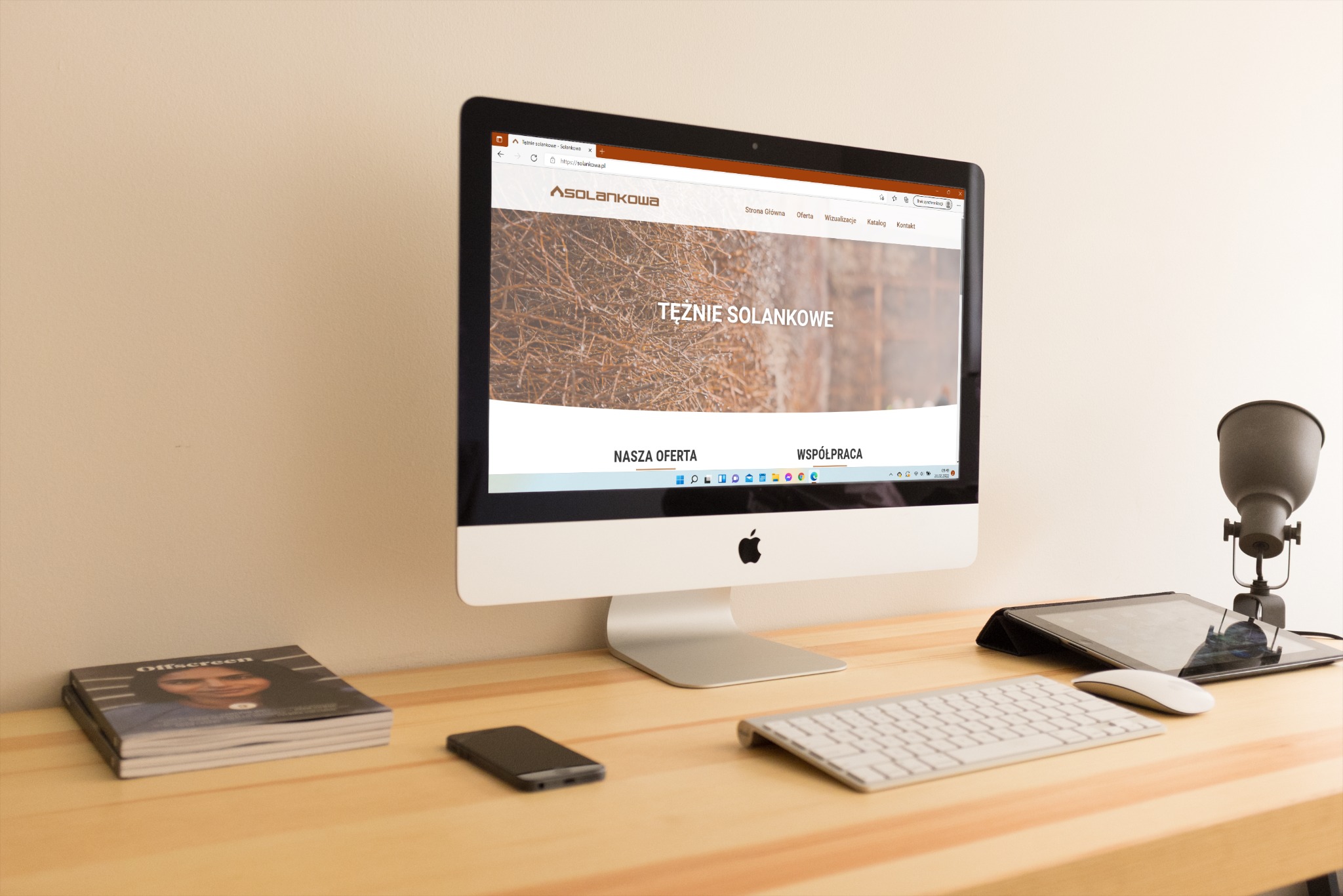 Ekran komputera iMac wyświetlający stronę internetową solankowa.pl z nagłówkiem 'Tężnie Solankowe', na biurku obok leżą: smartfon, klawiatura Apple, tablet w etui, myszka Apple oraz lampka biurkowa...